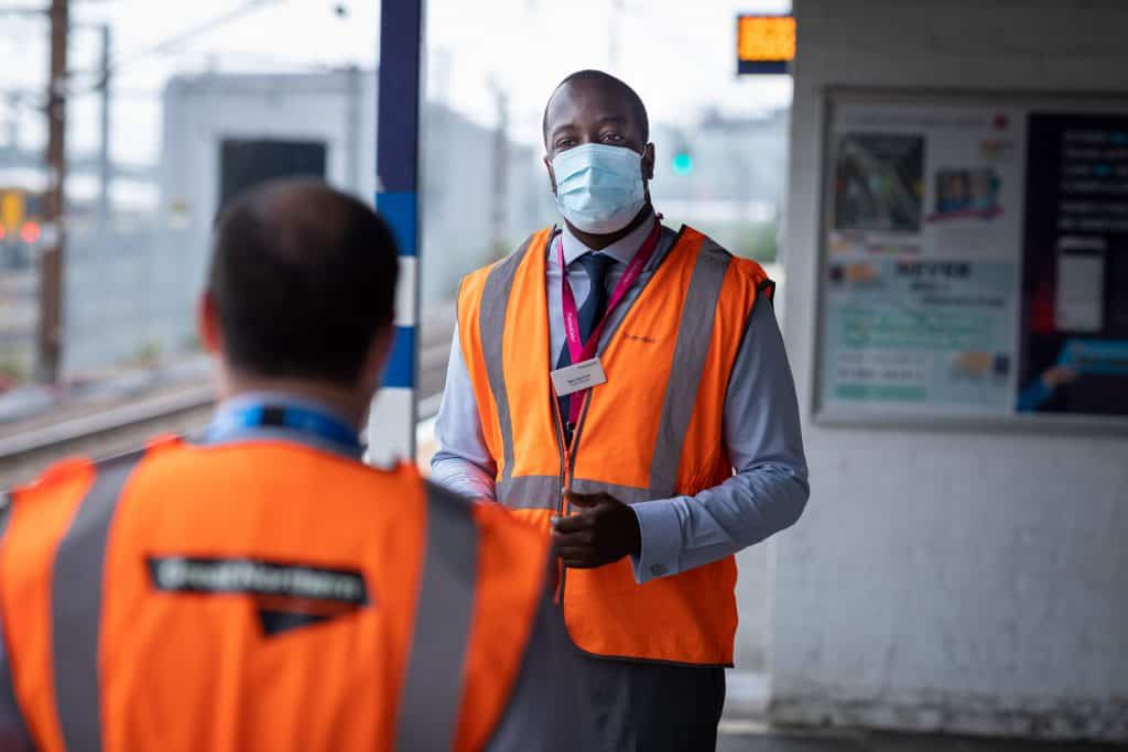 Male railway staff in face mask on train station talking to person