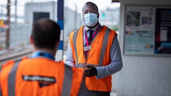Male railway staff in face mask on train station talking to person