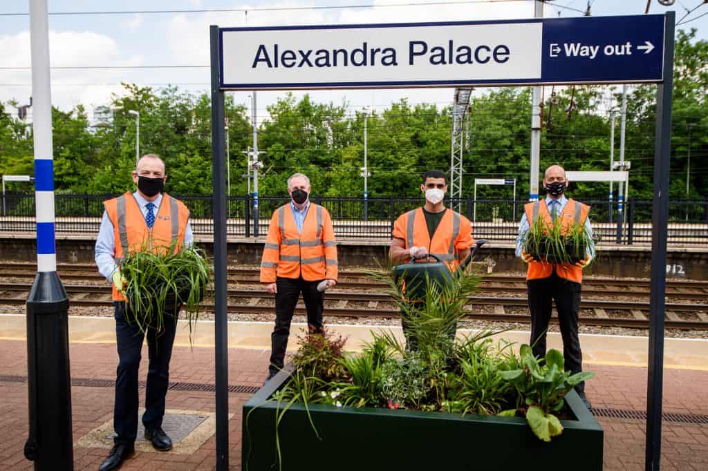 Four men in orange vests at railway platform with plants in their hands