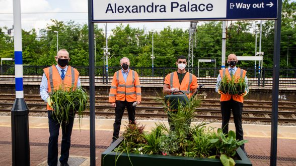 Four men in orange vests at railway station with plants in their hands