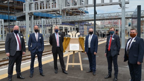 Men in suits and face masks unveiling a plaque at railway station