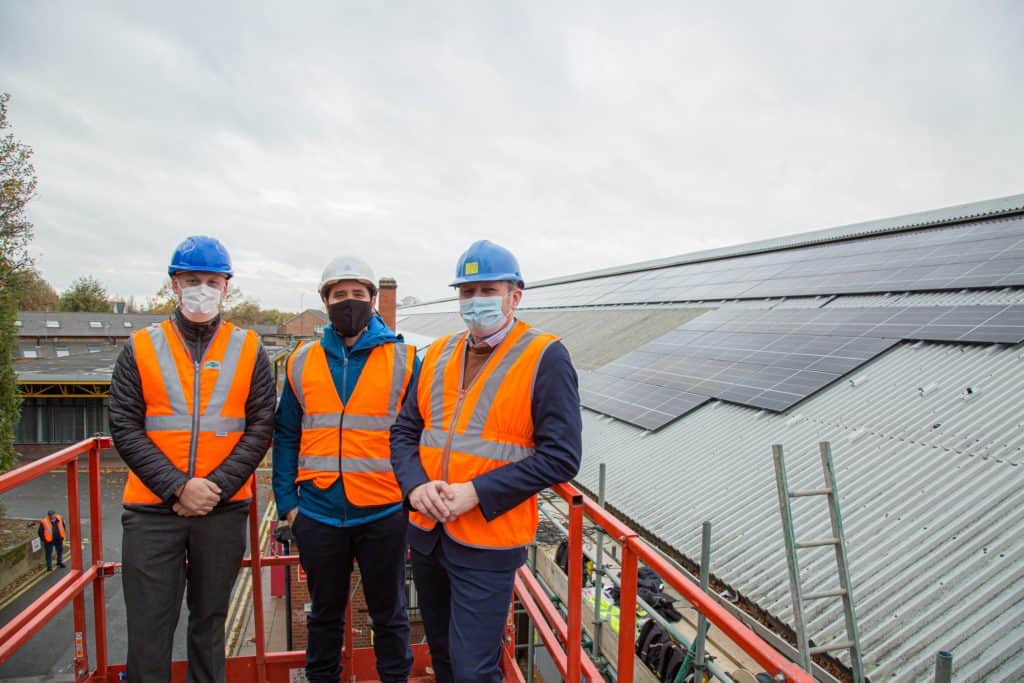 Men in high visibility vests and helmets standing by roof with solar panels