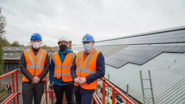 Men in high visibility vests and helmets standing by roof with solar panels